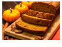 Sliced pumpkin bread loaf on wooden cutting board with pecans and small decorative pumpkins