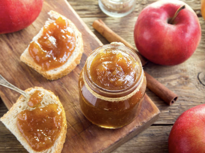 Jar of apple jam on a wooden board with jam-spread toast slices and whole apples