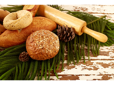 Assorted breads, rolling pin, and pine cones on evergreen sprigs over chipped wooden table