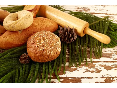 Assorted breads, rolling pin, and pine cones on evergreen sprigs over chipped wooden table