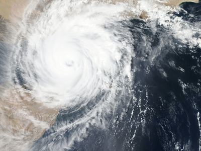 Large cyclone with distinct eye over ocean near a desert coastline.