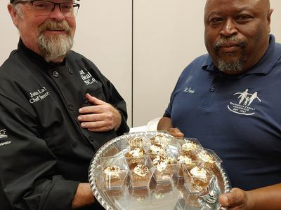 Two men holding a silver tray of individual dessert cups