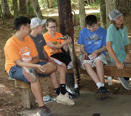 A group of kids inspect a pelt while sitting in an outdoor classroom at 4-H Camp.