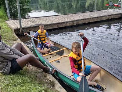 Two boys wearing life jackets paddling a canoe beside a wooden dock