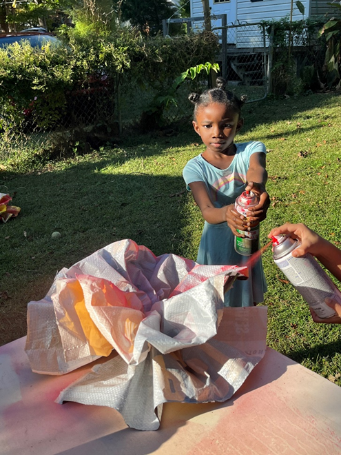 A young girl assists with spray painting paper into the color of flowers.