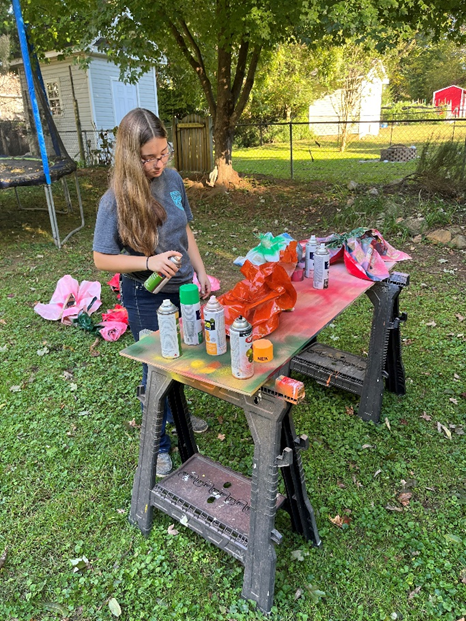 A girl spray paints paper into the color of various flowers.
