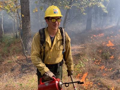 Image of Elliot Nauert holding a driptorch while managing a prescribed fire.