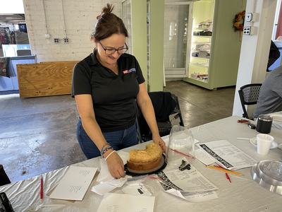Woman placing a partially sliced bundt cake on a table covered with papers and utensils
