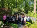 A ground of adults standing beneath a stone arch in a shaded garden.