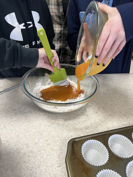 Students add a liquid pumpkin mixture to dry baking ingredients.