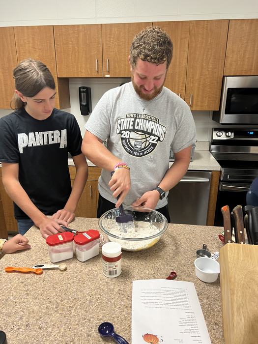 Two students mix ingredients for bread in a glass bowl.
