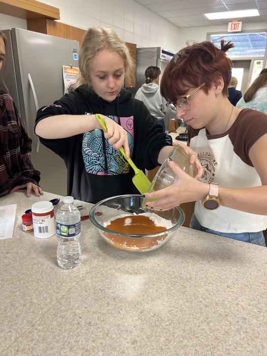 One student holds a bowl while another scrapes it empty.