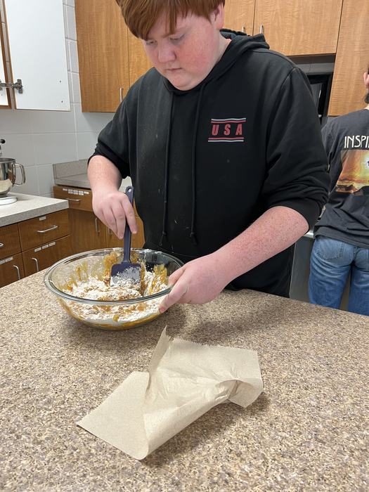 A student mixes the wet and dry ingredients for pumpkin bread.