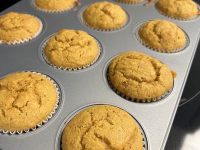 Golden-brown muffins in paper liners in a metal muffin tin on a stovetop