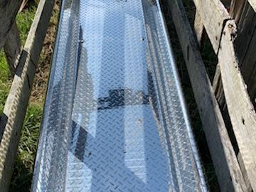 Aluminum diamond-plate loading ramp resting on wood between wooden fence panels