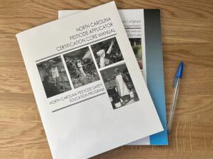 Stack of manuals titled "North Carolina Pesticide Applicator Certification Core Manual" and pen