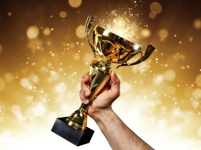 Hand holding a gold trophy cup raised against a sparkling golden background