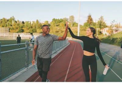 Two runners on a track giving each other a high-five, each holding a water bottle