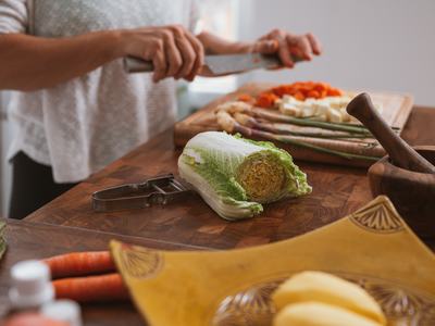 Hands slicing vegetables; halved napa cabbage on wooden cutting board