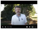 Man standing outdoors, wearing white polo with small "S" logo; video player controls visible