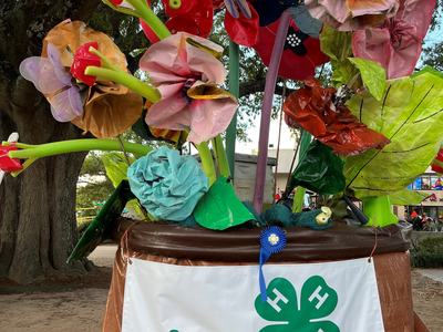 Large faux-flower display in planter with banner reading "4-H GROWS HERE"