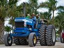 Blue Ford TW-20 tractor with driver and two children under palm trees
