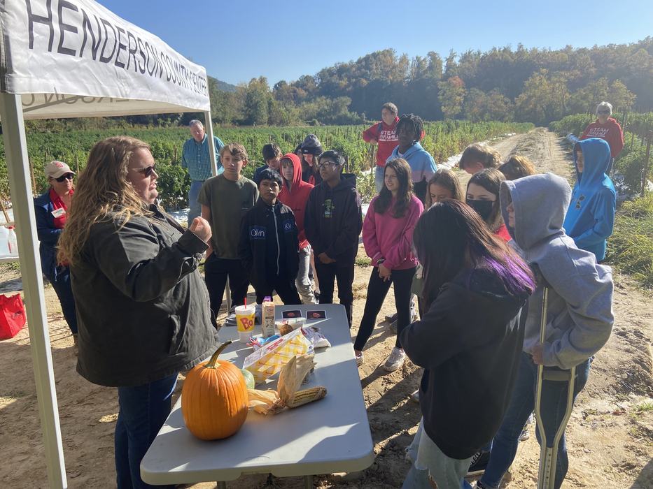 Students inspect a pumpkin under a tent.