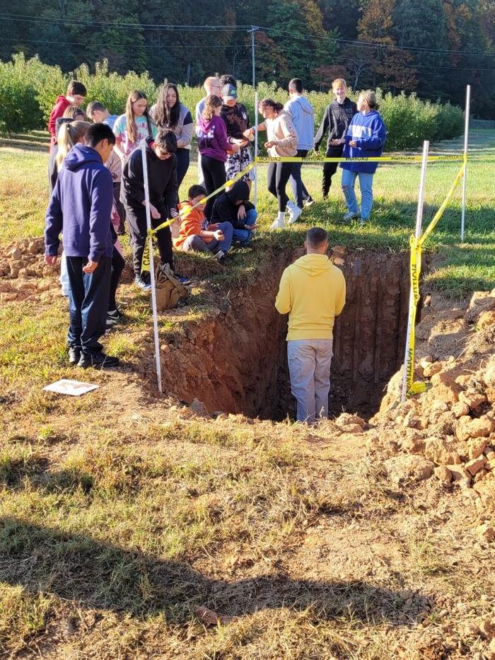 Students look on as a man inspects a hole.