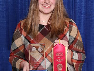 Person holding a glass trophy and red ribbon reading "SECOND PREMIUM High Individual Overall"