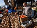 Man selecting tomatoes at an outdoor produce market stall with boxes of potatoes.