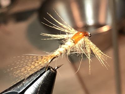 Hand-tied dry fly with orange body clamped in a fly-tying vise
