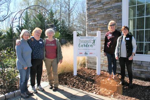 Volunteers smiling in front of Senior Enrichment Center Garden sign