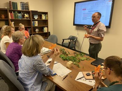 Instructor demonstrating flower parts to seated adults with orange lilies and leaves.