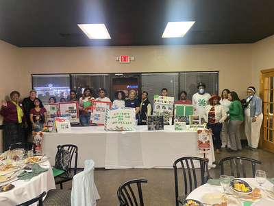 People standing behind a table with posters and sign: Pitt County 4H Allstars Club 25th Anniversary