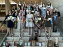 Group of young women on stairs holding plaques and ribbons, trophies displayed on steps below