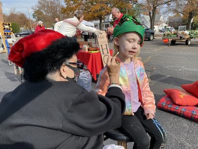 Woman painting a snowflake face design on a young girl's cheek at an outdoor market