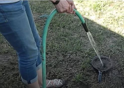 Gardener holding a hose that is spraying into a sieve full of soil on the ground.