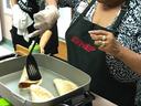 Two women wearing EFNEP aprons cooking folded tortillas on electric griddle