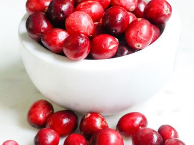 White bowl filled with red cranberries, extra cranberries scattered on a white surface
