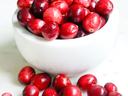 White bowl filled with red cranberries, extra cranberries scattered on a white surface
