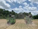 Two green tractor-mounted planters driving across a dusty field planting rows