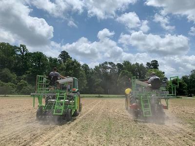 Two green tractor-mounted planters driving across a dusty field planting rows
