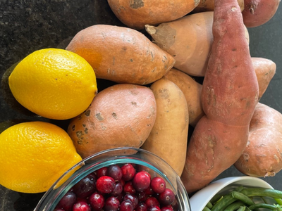 Sweet potatoes, two lemons, bowl of cranberries and green beans on dark countertop