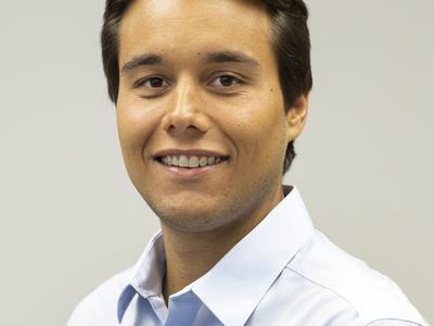 Young man in light blue dress shirt, headshot on plain gray background