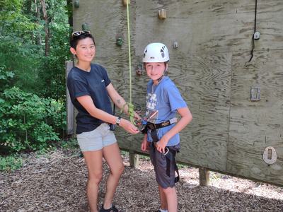 Camp counselor secures harness on child wearing helmet at outdoor climbing wall