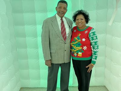 Man in gray suit with red striped tie and woman in red Christmas sweater in green-lit inflatable booth