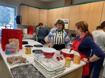 Four women cooking in a community kitchen, two women mixing ingredients at a counter