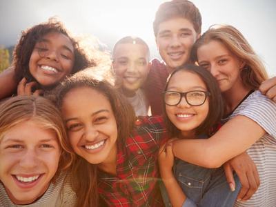 Seven teenagers huddled closely, smiling at camera outdoors