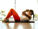Woman in orange leggings doing abdominal crunches on a mat in a gym by a window