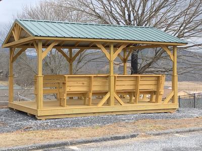Wooden pavilion with built-in benches and green metal roof on raised platform